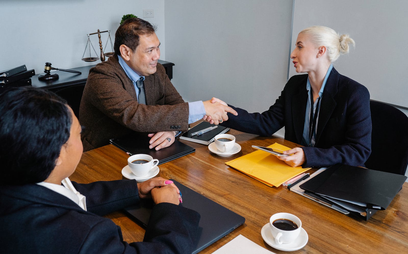 Businesspeople in formal wear sitting at table with documents and coffee while shaking hands after successful business deal