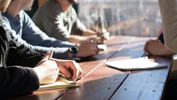 people sitting on chair in front of table while holding pens during daytime