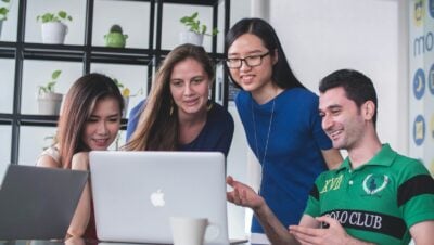 four people watching on white MacBook on top of glass-top table