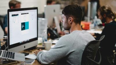 man in gray sweatshirt sitting on chair in front of iMac